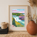 a painting of a waterfall in a frame next to a potted plant