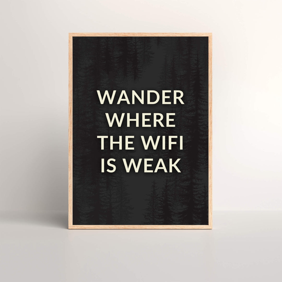 a wall art print with the saying 'Wander Where The Wifi is Weak' in a oak picture frame with black and white text