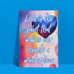Fine Art Giclee Print - Love is the paint that makes our hearts a masterpiece - leaning up against a blue wall.